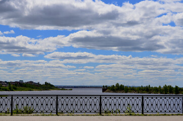 Fence on the embankment by the river under the blue sky with clouds