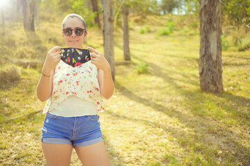 Casual woman portrait wearing face mask in forest or Park. Portrait of young happy woman with face...