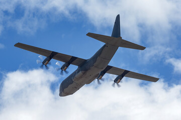 Large C-130 cargo plane used by the military flying against a partly cloudy sky.