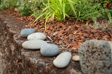River Rocks on a Stone Retaining Wall with Red Bark Chips and Green Plants
