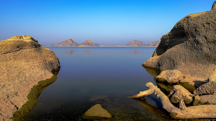 A selective focus image of a  landscape of Jawai dam with clear blue sky and Aravalli mountain ranges with its reflection in water at Jawai in Rajasthan  India