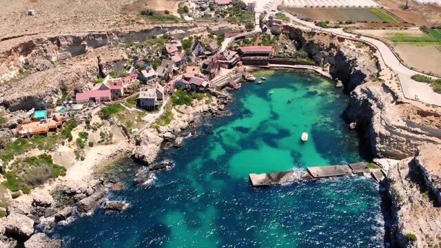 Beautiful small fishing village aerial birds eye shot fly backward bay reveal. Popeye village filming location, Malta.