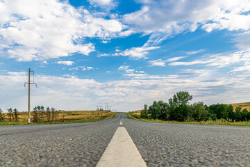 The asphalt road goes into the horizon. Blue sky and clouds