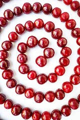 Red cherry ripe juicy is laid out in a spiral on a white background.