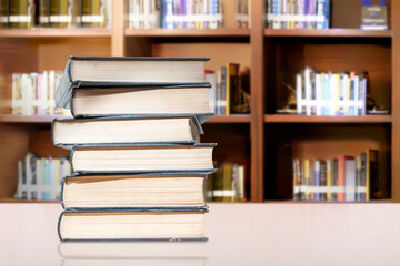 Desk with a stack of books with bookshelf background