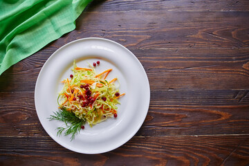 Fresh cabbage salad made from shredded white cabbage, carrots and berries on a white plate. Top view, wooden background, selective focus