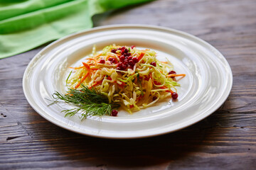 Fresh cabbage salad made from shredded white cabbage, carrots and berries on a white plate. Top view, wooden background, selective focus