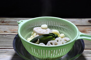 Sliced or cutting peeled Lotus root, fresh truffle and bunch of green Pandan leaves in the plastic basket. Boiled traditional vegetable in Thailand with pandan leaf for making dessert. 