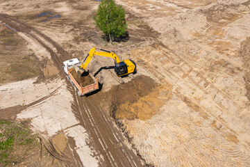 yellow excavator loading a dump truck on construction site. aerial view