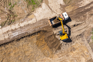 industrial excavator loading ground into a dump truck on construction site. aerial top view