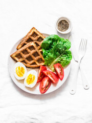 Savory zucchini waffles, boiled egg, fresh organic tomatoes, romano salad on a light background, top view.  Healthy breakfast