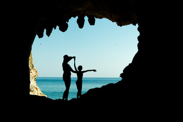 mamma e figlia in silhouette dentro una grotta con lo sfondo del mare e il cielo azzurro