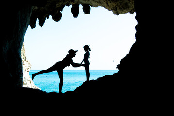 mamma e figlia mamma e figlia in silhouette dentro una grotta con lo sfondo del mare e il cielo...