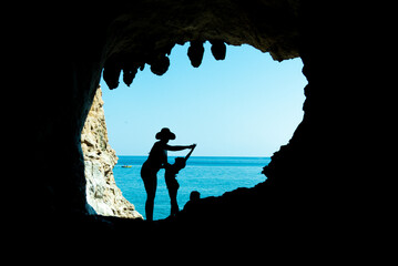 Mamma e figlia in silhouette dentro uina  grotta si divertono. Dietro il cielo e il mare del...