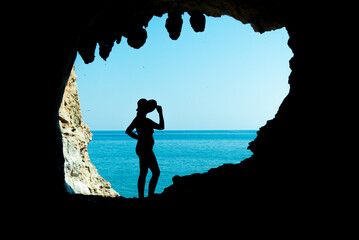 ragazza in silhouette dentro una grotta con lo sfondo del mare e il cielo azzurro