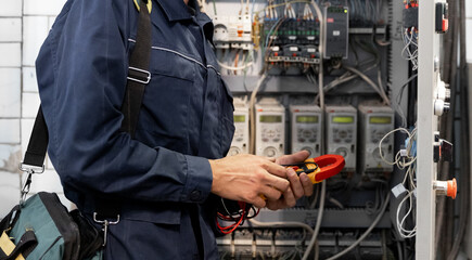 Electrician engineer checks electrical circuit in control panel for high current and voltage,...