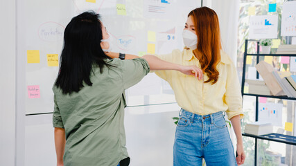 Asia businesspeople greeting with elbow bump and wear medical face mask for social distancing in new normal situation for virus prevention back at work in office. Lifestyle and work after coronavirus.
