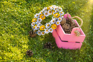 Hand-made pine cone wreath with pink box and pine cones under sun beams during golden hour.