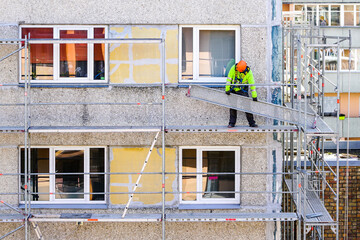 the worker assembles the scaffolding on the facade of a multi-storey house at a dangerous height