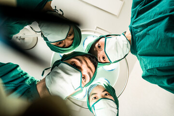 Professional medical team performing surgical operation in modern operating room. Low view angle from patient when surgeons doctor work during operation on intensive care patient in hospital.