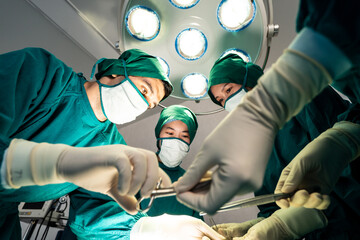 Professional medical team performing surgical operation in modern operating room. Asian assistant hands out instruments to surgeons doctor during operation on intensive care patient in hospital.