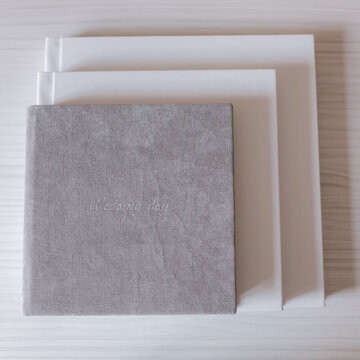 Different photobooks and photoboxes on white wooden table. Textile and leather. Comparison between 20x20, 25x25 and 30x30