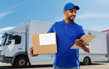 mail service and shipment concept - happy indian delivery man with parcel box and clipboard in blue uniform over truck on street background