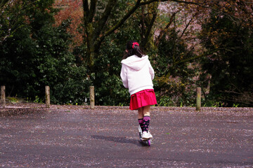 Fototapeta na wymiar 公園の駐車場でキックボードで遊ぶ女の子
