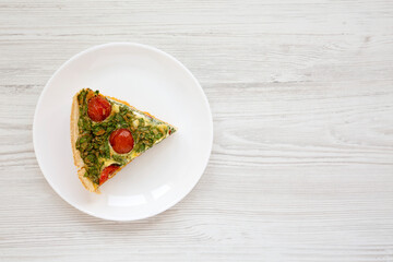 A Piece of Homemade Spinach Quiche on a white plate on a white wooden background, top view. Flat lay, overhead, from above. Space for text.