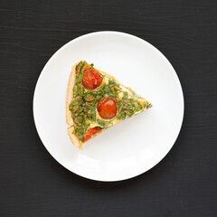 A Piece of Homemade Spinach Quiche on a white plate on a black surface, top view. Flat lay, overhead, from above.