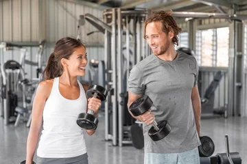 Tuinposter Fitness gym personal trainer coach training Asian woman with free weights dumbbell bicep curls workout talking having fun exercise partner. Fit man, happy girl. © Maridav