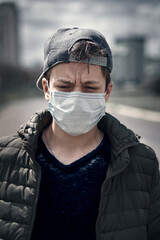 teenage boy poses in a city street, wearing a protective face mask - the concept of modern life and virus protection
