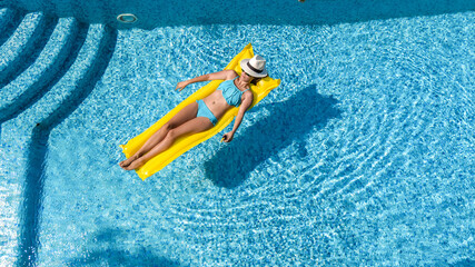 Beautiful young girl relaxing in swimming pool, woman swims on inflatable mattress and has fun in water on family vacation, tropical holiday resort, aerial drone view from above
