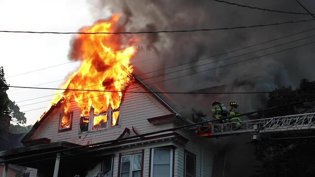 The Roof of a Wooden House Engulfed in Flames with Firefighters on the Scene