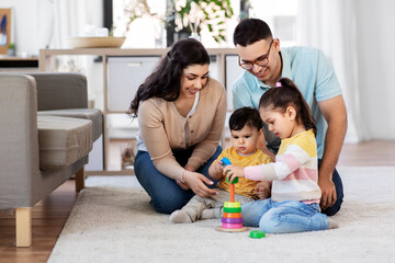 family and people concept - happy mother, father, little daughter and baby son playing with pyramid toy at home