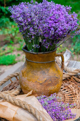 Rustic still life with lavender. A large bouquet of lavender in an old handicraft clay jug on the background of a garden in Ukraine. Bouquet of lavender in kraft paper near the jug. Vertical image.