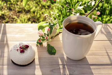 Beautiful porcelain coffee cup with mousse pastry dessert decorated with pink apple tree branches in bloom on wooden table. Spring garden in setting sun light.