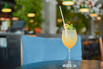 Cold summer alcohol cocktail with ice and orange in a tall glass on wooden table on blurred restaurant background.