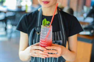 Attractive young woman waiter holding red colorful refreshing cocktail with ice and lime. Fruit tropical mix drink.