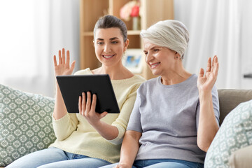 family, generation and technology concept - happy smiling senior mother and adult daughter with tablet pc computer having video call at home
