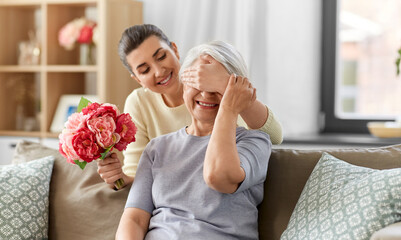 family, mother's day and birthday concept - happy smiling adult daughter giving flowers to her senior mother at home