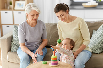 family, generation and female concept - happy smiling mother, baby daughter and grandmother playing with toy pyramid at home