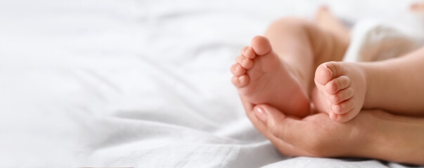 Mother holding feet of her little baby on bed, space for text. Banner design