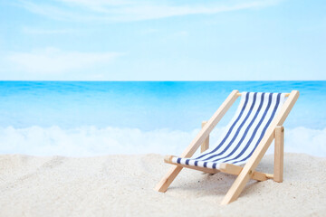 Blue and white deck chair on white sand beach with blurred blue sea and sky