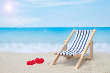 Two red hearts and deck chair on white sand beach with blurred blue sea and sky