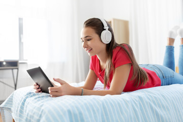 children, technology and communication concept - smiling teenage girl in headphones listening to music on tablet computer at home