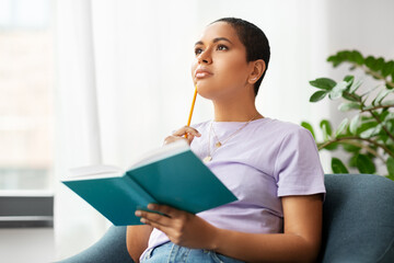 people and leisure concept - african american woman with diary and pencil sitting in chair at home