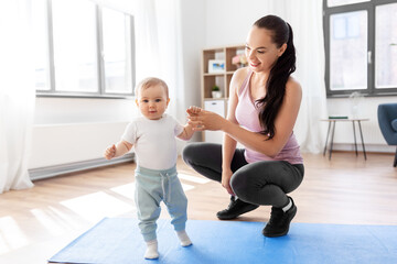 Fototapeta na wymiar family, sport and motherhood concept - happy smiling mother with little baby sitting on exercise mat at home