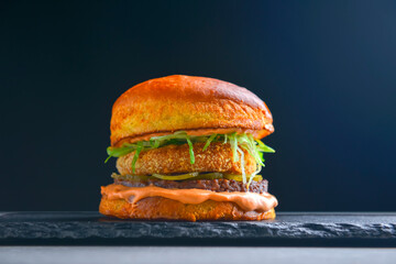 Juicy delicious craft burger with spices on a black background. Fast food, junk food concept.