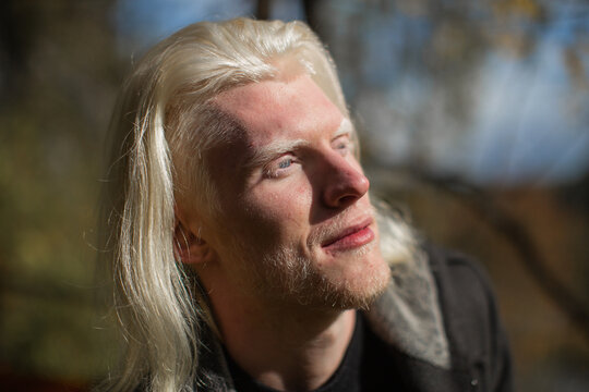 Photo in profile of a young man with a rare appearance of an albino with long hair and a beard, on his face fall bright sunlight